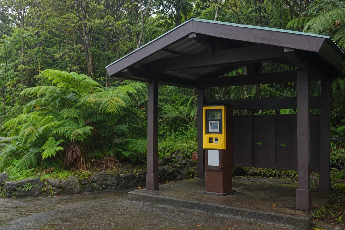 Card-only self-pay fee kiosk at the ʻAkaka Falls State Park parking area surrounded by tropical greenery