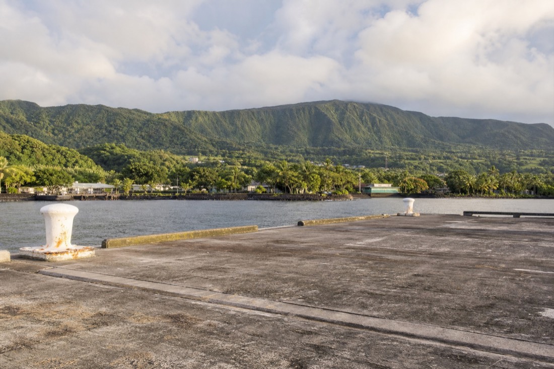 Empty concrete pier apron at Hilo Harbor in early morning light with mooring bollards and the green Hamakua ridgeline beyond