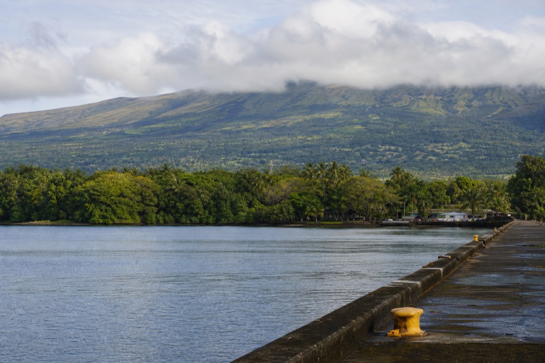 Early morning at the Hilo cruise pier with calm bay water and the green slope of Mauna Kea behind low cloud