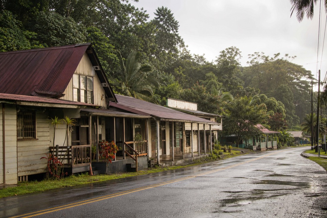 Quiet plantation-era wooden storefronts along the main street in Honomu on the Hamakua Coast, early morning light, wet road after overnight rain