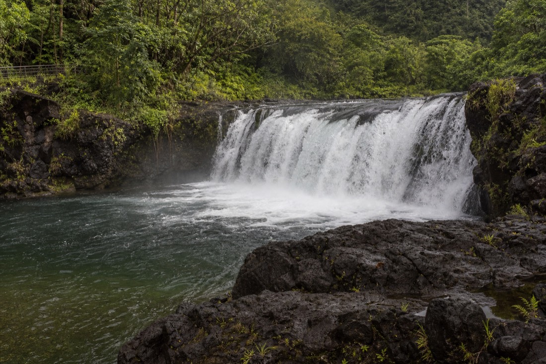 Wide low waterfall spilling over a lava ledge into a pool on the Wailuku River in Hilo with mist rising