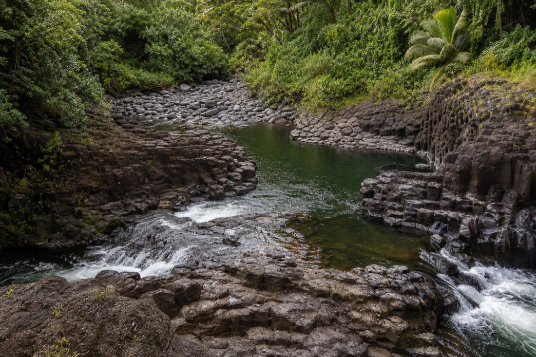 Hexagonal basalt columns and deep river pools at Boiling Pots on the Wailuku River with rainforest crowding both banks